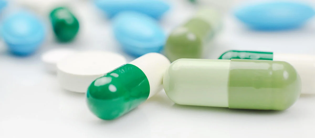 Nahaufnahme von grünen und weißen Kapseln sowie blauen und weißen Tabletten auf weißem Hintergrund, medizinische Medikamente