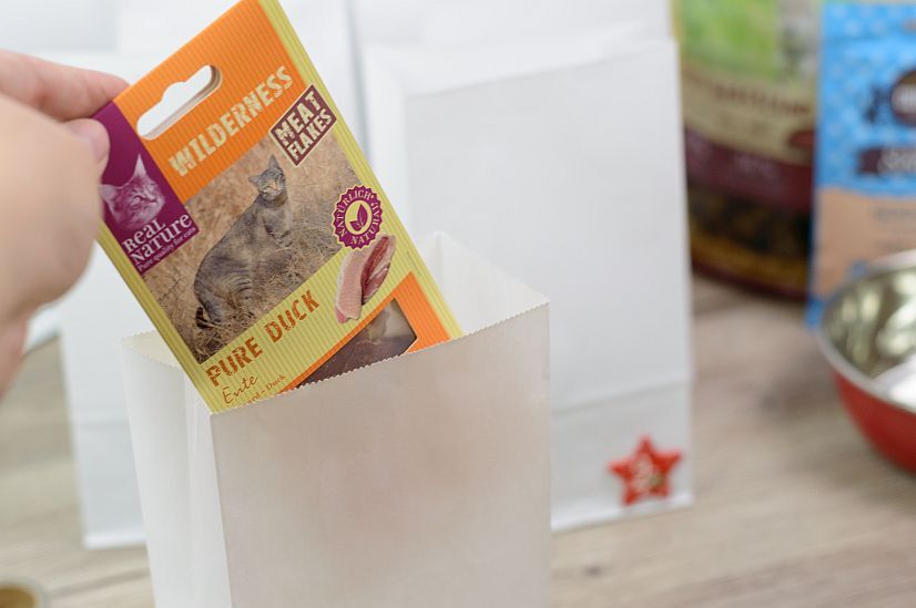 Schritt3 Main mettant un sachet de friandises pour chat Real Nature Wilderness Meat Flakes Pure Duck dans un sac en papier blanc
