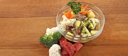 Hausgemachter Rindfleisch-Gemüseeintopf mit Brokkoli, Blumenkohl, Kartoffeln und Karotten in Glasschüssel auf Holztisch