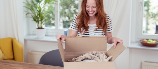 Jeune femme souriante ouvrant un colis avec du papier d'emballage dans un salon lumineux