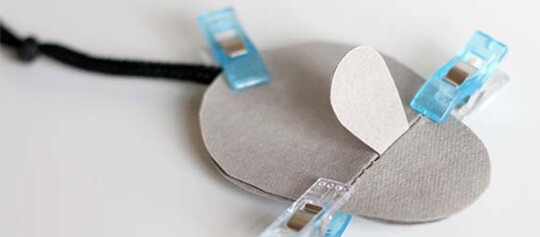 Nahaufnahme eines Nähprojekts mit grauen Stoffstücken, die mit blauen und transparenten Clips zusammengehalten werden.