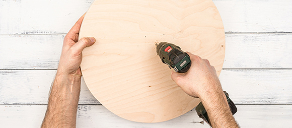 DIY_Futterbaum_Beitrag_03_1200x527 Person bohrt mit Akku-Bohrmaschine in eine runde Holzplatte auf weißem Holzhintergrund, DIY-Holzarbeit