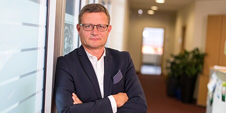 Geschäftsmann mit Brille und blauem Anzug steht selbstbewusst im Büroflur mit verschränkten Armen