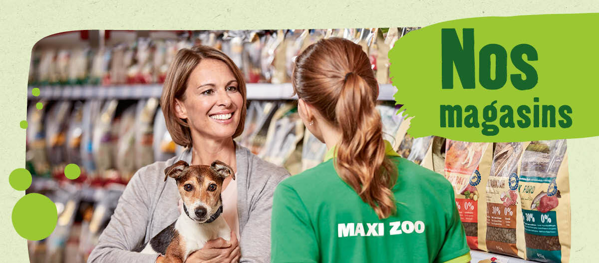 Interaction conviviale entre une cliente tenant un chien et une employée du magasin Maxi Zoo devant des rayons de nourriture pour animaux.