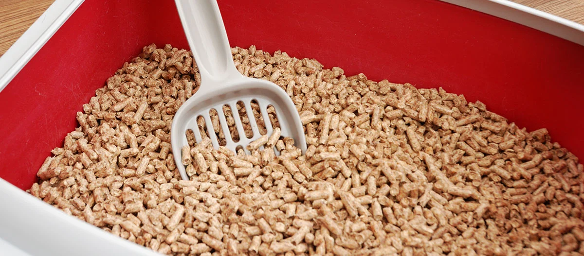 Brown pellet cat litter in red litter box with white plastic scoop