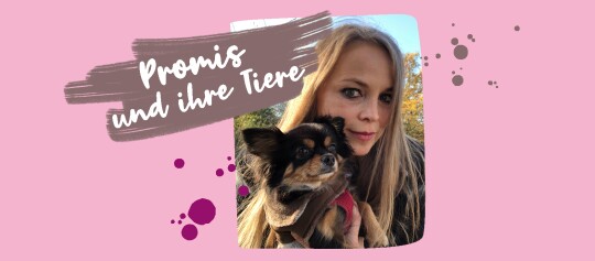 Promis und ihre Tiere – Frau mit langem blondem Haar hält kleinen schwarz-braunen Hund im braunen und roten Outfit im Freien