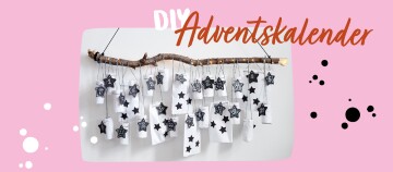 DIY Adventskalender aus einem Ast mit weißen Papiertüten und schwarzen Sternanhängern, nummeriert von 1 bis 24, hängend an einer Wand.