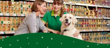 Dwie kobiety i golden retriever w sklepie zoologicznym, doradztwo przy zakupie karmy dla psa na tle półek z produktami.