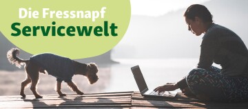 Frau arbeitet am Laptop auf einem Steg am Wasser, kleiner Hund mit Pullover neben ihr, Fressnapf Servicewelt Banner