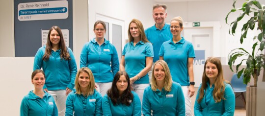 Teamfoto der Tierarztpraxis Dr. René Reinhold mit freundlichen Mitarbeitern in türkisfarbenen Uniformen in einer modernen Praxis.