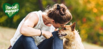 Frau zeigt liebevolle Zuneigung zu ihrem Hund im Freien, Herz mit Schriftzug
