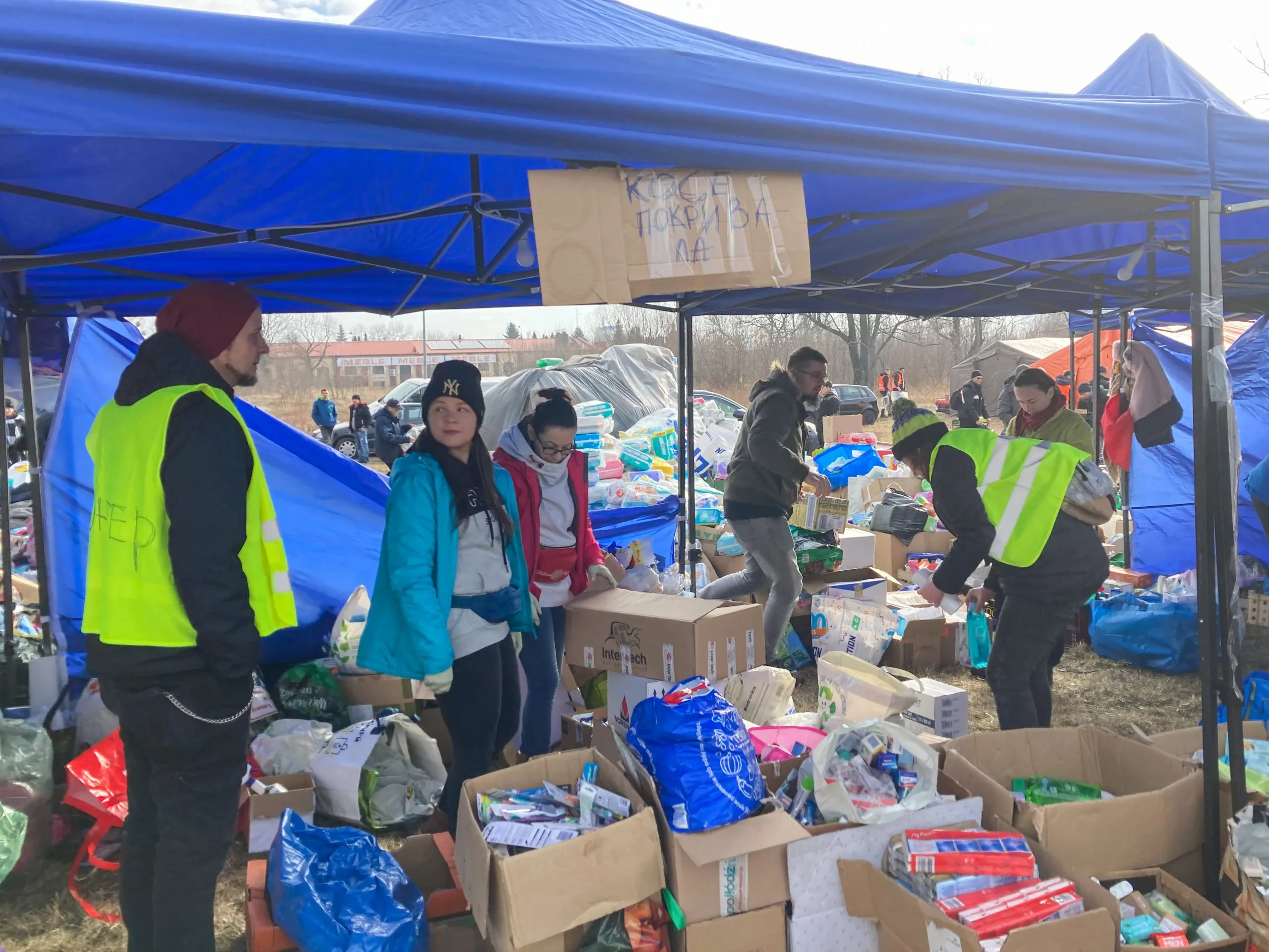 Freiwillige organisieren Hilfsgüter unter einem blauen Zelt bei humanitärer Hilfe mit Hygieneartikeln und Lebensmitteln.