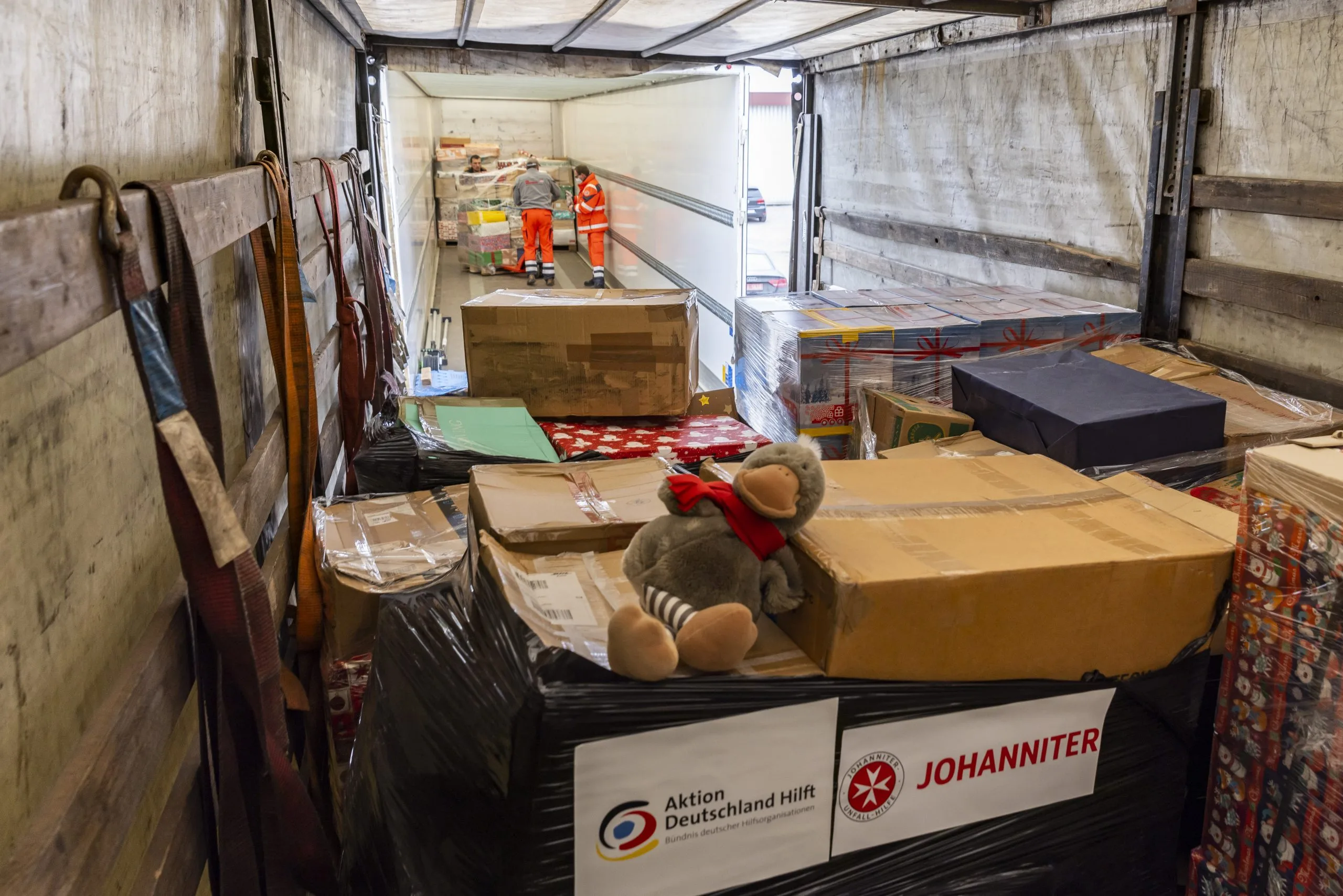 LKW-Ladung mit Hilfspaketen und Plüschtier, Aktion Deutschland Hilft und Johanniter humanitäre Hilfe, Arbeiter im orangefarbenen Sicherheitsanzug laden Pakete.