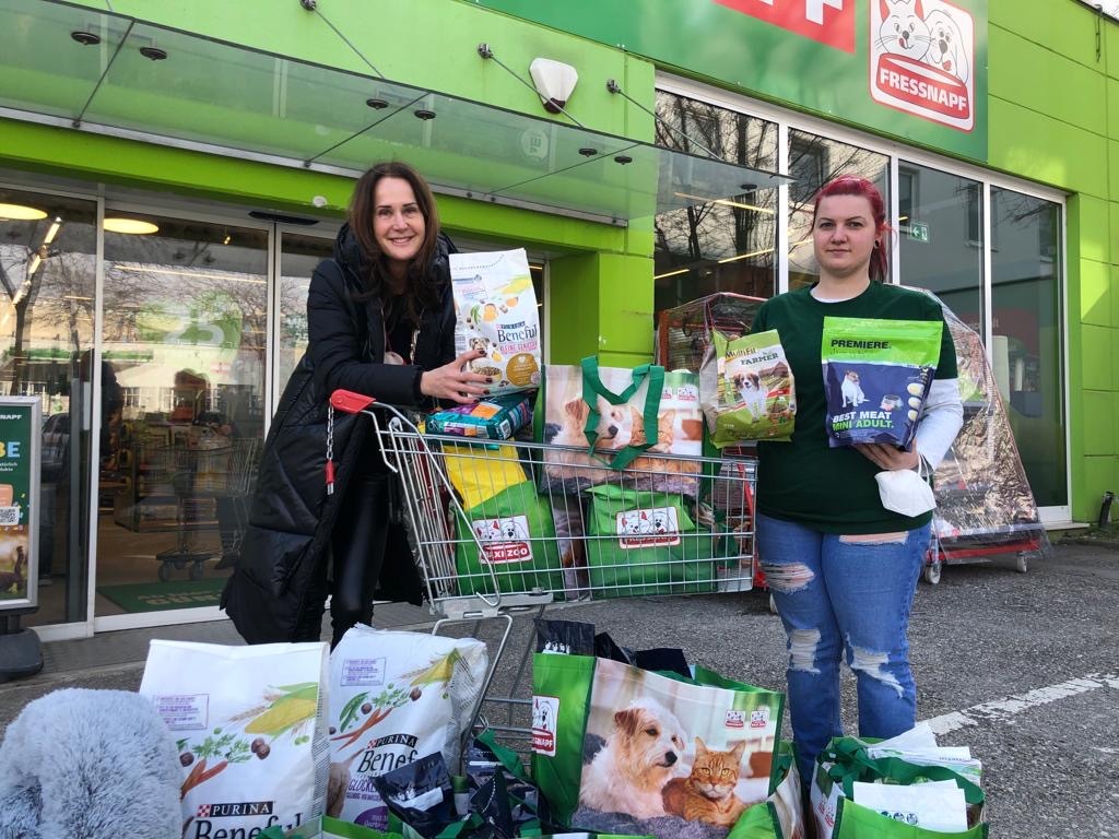 Zwei Frauen vor einem Fressnapf-Tiergeschäft mit Einkaufswagen und mehreren Tüten voller Tiernahrung und Haustierbedarf.
