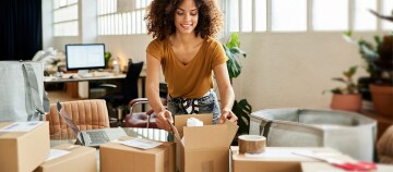 Junge Frau packt Kartons in einem modernen Büro, Versand und Verpackung im Homeoffice