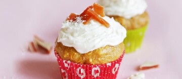 Zwei Cupcakes mit weißem Frosting und getrockneten Fruchtstücken, einer in rotem und einer in grünem Papierförmchen, auf rosa Untergrund.