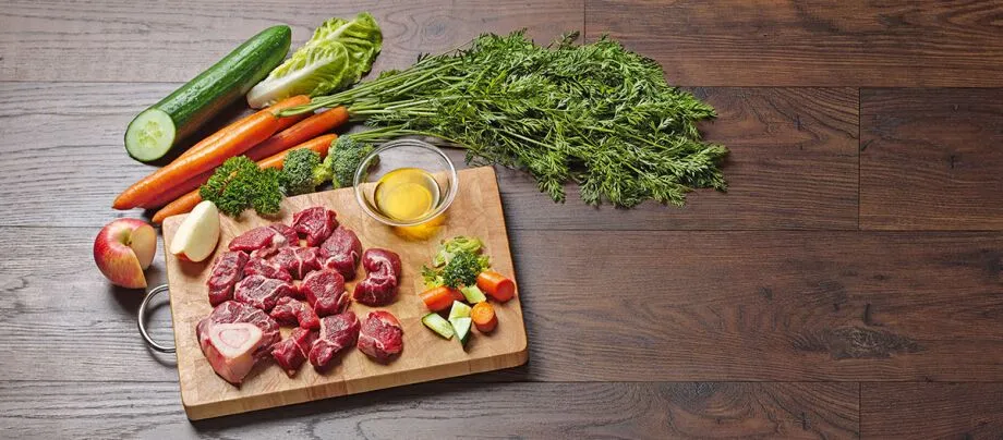 Frisches rohes Fleisch mit Karotten, Gurke, Apfel und Kräutern auf einem Holzbrett auf einem Holztisch