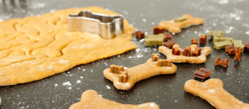 Hausgemachte Hundekekse in Knochenform mit Hundeleckerlis auf dunkler, bemehlter Arbeitsfläche