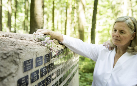 Frau legt Blumen an eine Gedenkwand im Wald, um verstorbene Angehörige zu ehren.