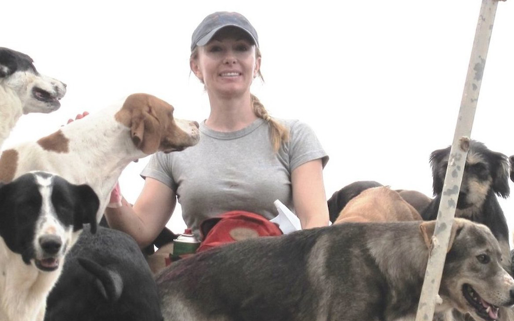 Femme en t-shirt gris et casquette, entourée de plusieurs chiens dans un environnement extérieur amical