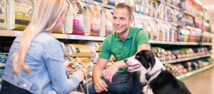 Employé amical conseille une cliente dans le rayon nourriture pour animaux avec un chien à proximité