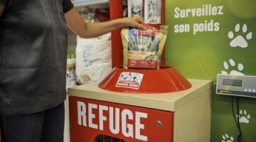 Personne déposant un sac de nourriture pour animaux dans une boîte de don rouge pour refuge, mur vert avec empreintes de pattes et texte « Surveillez son poids » en arrière-plan