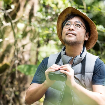 Man met strohoed en verrekijker die vogels bekijkt in een groen bos
