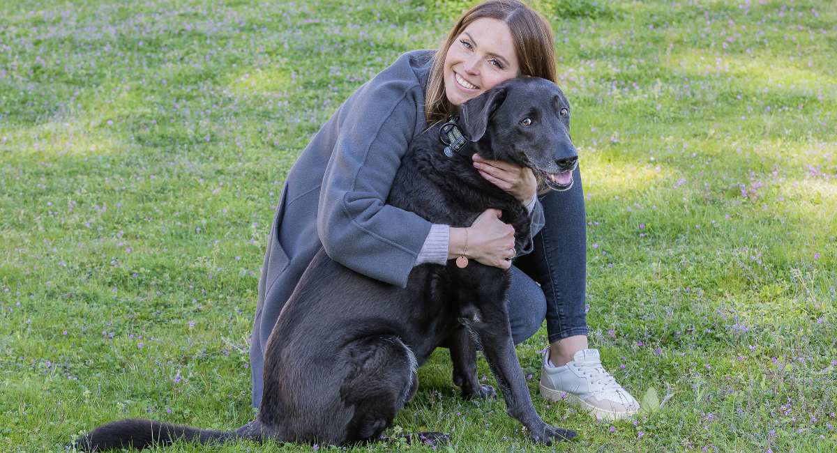 Blije vrouw die grote zwarte hond omhelst op bloeiende weide in het park