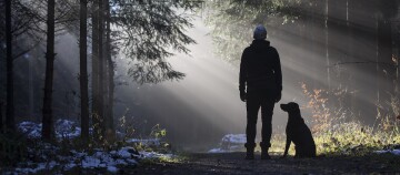 Frau steht mit Hund im Winterwald