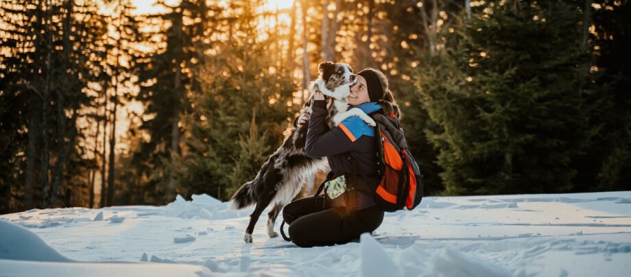 Eine Frau kniet mit ihrem Hund im Schnee