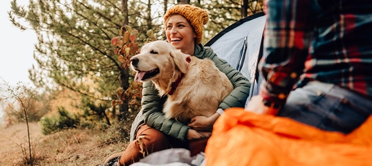 Glückliche Frau mit goldenem Retriever beim Camping im Wald, entspannte Naturerfahrung im Freien