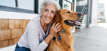 Gelukkige oudere vrouw knuffelt haar blije Golden Retriever hond buiten in de stad