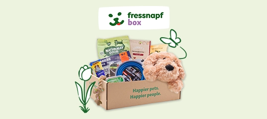 Fressnapf Box mit Haustierprodukten, inklusive Plüschhund, Futter, Leckerlis und Zubehör, auf hellem Hintergrund mit Blumenillustrationen