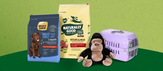 Twee zakken hondenvoer, een knuffelgorilla en een paarse dierenvervoersbox op een groene achtergrond