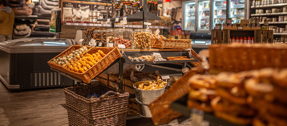 Gemütlicher Feinkostladen mit Körben voller Brezeln, Brotstangen und handgemachten Backwaren auf Holzregalen.