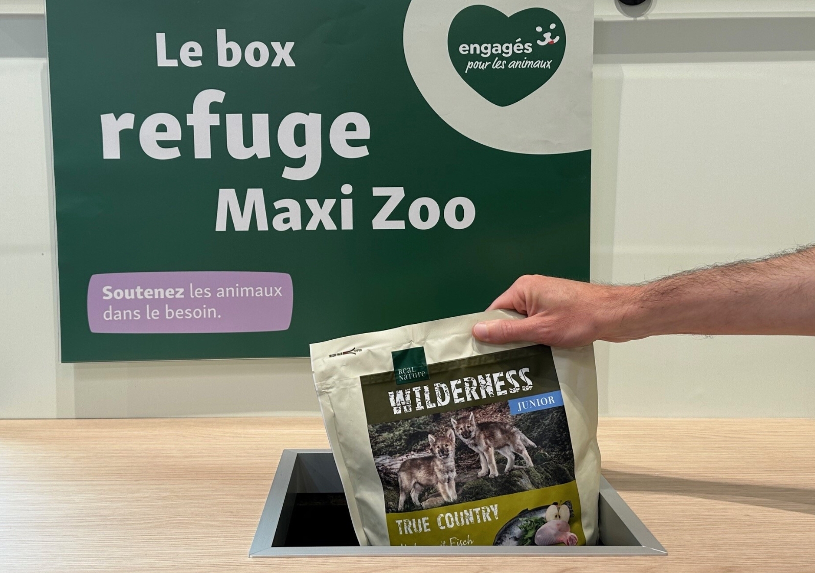 Une main dépose un paquet de nourriture pour animaux Wilderness Junior dans la boîte de don 
