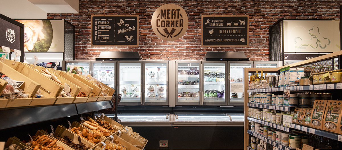 Meat Corner im Tierfachgeschäft mit natürlichen und biologischen Fleischprodukten für Haustiere, gekühlten Verpackungen und Holzregalen mit Snacks und Nahrungsergänzungsmitteln