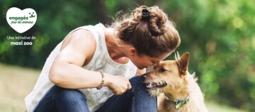 Femme assise dans un parc montrant de l'affection à son petit chien marron, engagée pour les animaux, initiative de Maxi Zoo.