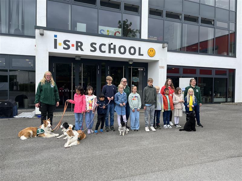 Gruppe von Kindern und Erwachsenen mit Hunden vor der i-S-R School, freundliche Schulveranstaltung mit Tieren