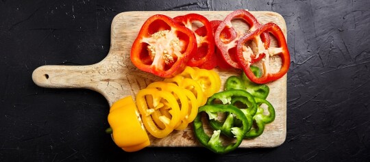 Rote, gelbe und grübe Paprika liegt aufgeschnitten auf einem Schneidebrett