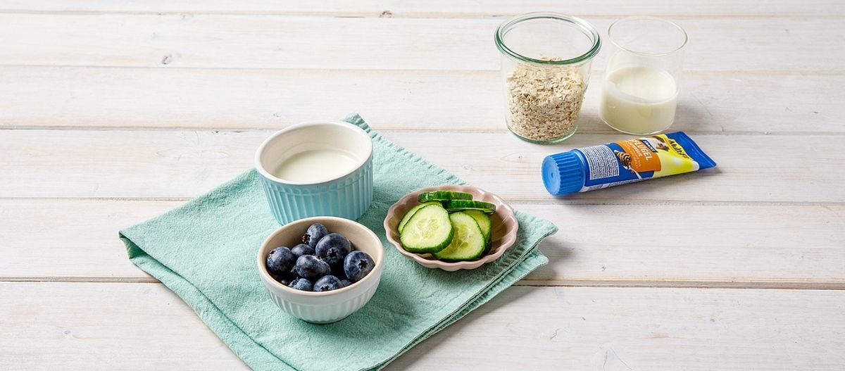 Ratgeber-Hund-DIY-Hunde-Rezept-Füllung-fue-Schleckmatte-Zutaten_1200x527 Auf einem Tisch stehen verschiedene Schalen mit Gurken, Heidelbeeren, Joghurt und Haferflocken, sowie eine Hundeleberwurst-Paste