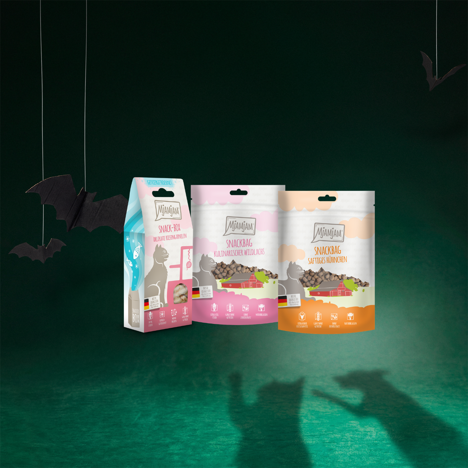 On voit ici trois friandises pour chats : la « Snackbox Crevettes géantes » de 25 g, le « Snackbag Saumon sauvage gastronomique » de 125 g et le « Snackbag Poulet juteux » de 125 g, tous de la marque MjAMjAM.