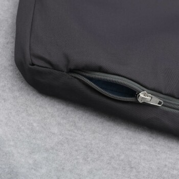 Nahaufnahme eines dunkelgrauen Haustierbettes mit einem teilweise geöffneten Reißverschluss, das auf einer weichen grauen Oberfläche ruht.