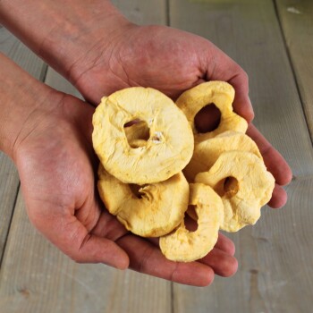 Hände halten mehrere getrocknete Apfelringe auf einer Holzoberfläche, Tierleckerei aus einem Online-Shop.