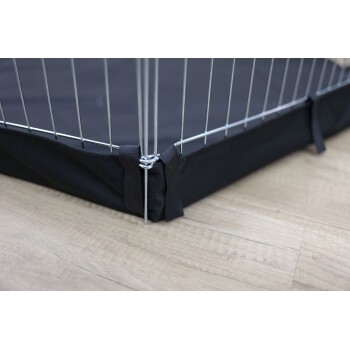 Nahaufnahme einer Ecke einer Haustierbox mit einem schwarzen Stoffboden und einem Metallgitterrahmen, der sichere Bindungen und einen Holzboden im Hintergrund zeigt.