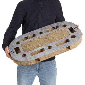 Eine Person hält ein großes, ovales Katzenkratzbrett mit einer strukturierten Oberfläche und mehreren Ausschnitten, das für das Spiel von Haustieren konzipiert ist.