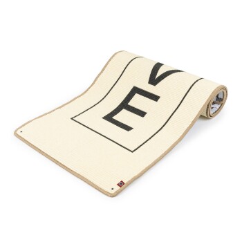 Eine gerollte Haustiertrainingsmatte mit einer cremefarbenen Oberfläche, die einen großen schwarzen Buchstaben "E" und einen beigen Rand zeigt, entworfen für das Training von Haustieren.