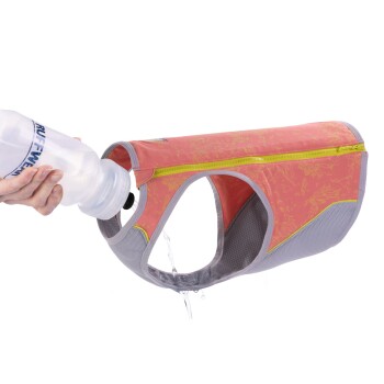 Eine Hand hält eine Wasserflasche, die Wasser in eine pinke Hundehydrationsweste mit grauen Mesh-Seiten und einem gelben Reißverschluss gießt.