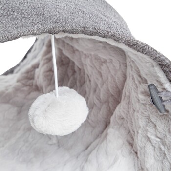 Ein gemütliches Haustierbett mit einem weichen, plüschigen Innenraum und einem grauen Stoffaußenbereich, mit einem baumelnden, flauschigen Pom-Pom-Spielzeug.