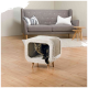 Eine getigerte Katze schaut aus einem gemütlichen, modernen Katzenhaus mit einem weichen Innenraum und einer Kratzbaumseite, das in einem stilvollen Wohnzimmer steht.
